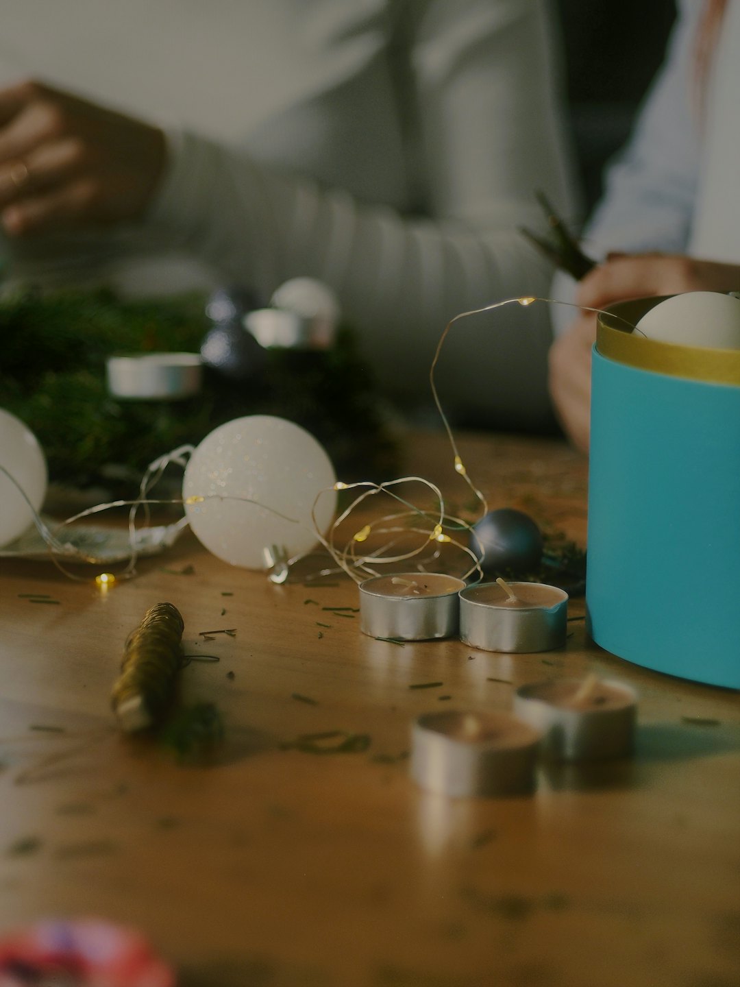 Two people working on holiday crafts at a wooden table.