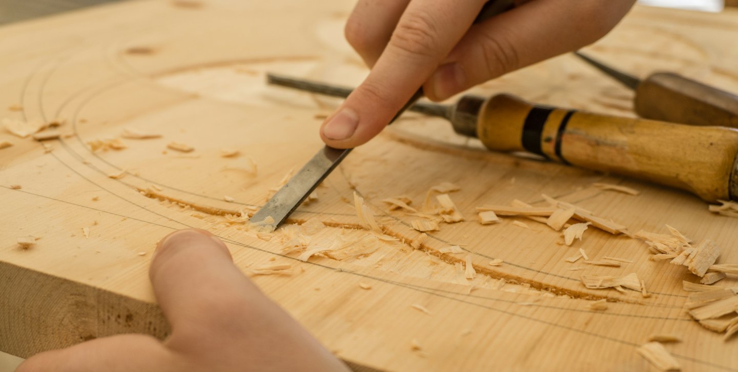 Hands using a chisel to carve wood.